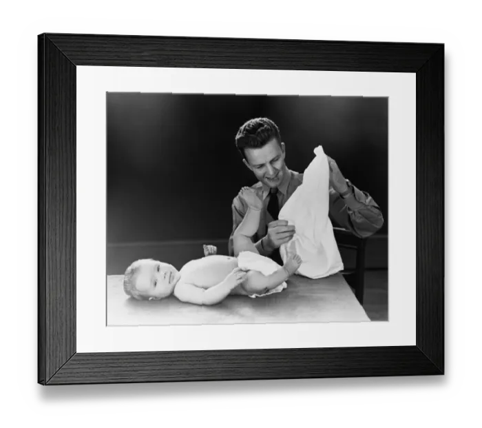 Framed Print : Young father with baby lying on table, trying to figure out how to put on diaper. (Photo by H Framed Print : Young father with baby lying on table, trying to figure out how to put on diaper. (Photo by H