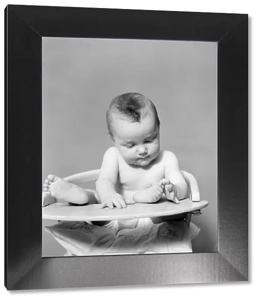 Baby with feet propped up on highchair tray, playing with toes