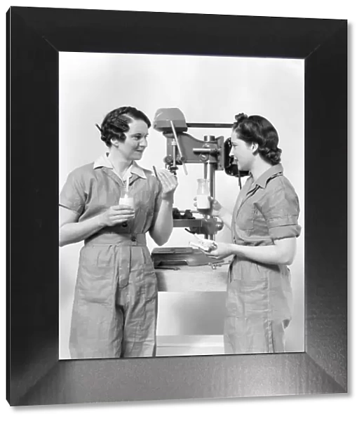 Two women workers standing near drill press, eating sandwich and drinking milk
