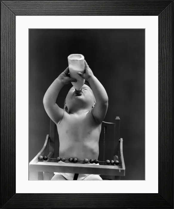 Framed Print : Baby sitting in high chair, head tilted back, drinking from milk bottle. (Photo by H Framed Print : Baby sitting in high chair, head tilted back, drinking from milk bottle. (Photo by H