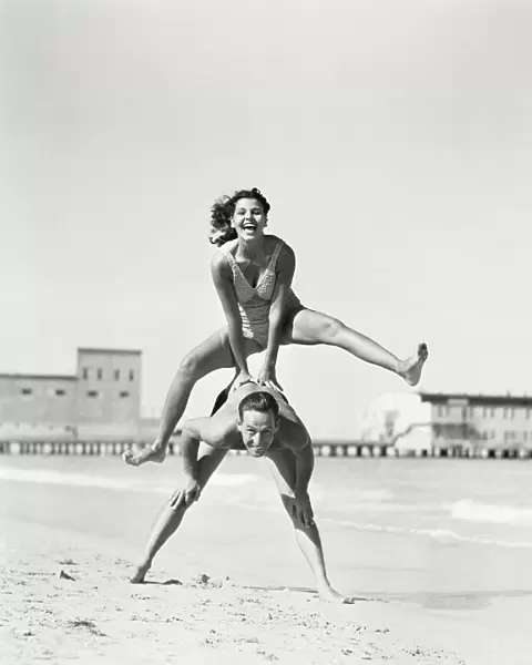 Couple playing leapfrog on beach, woman jumping over man