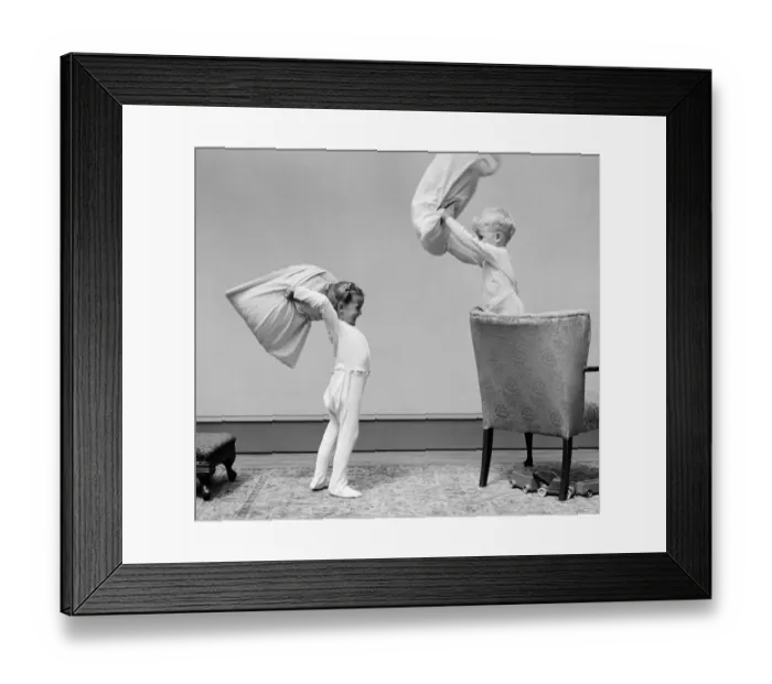 Framed Print : Boy and girl having a pillow fight, boy standing on chair swinging pillow, girl on floor Framed Print : Boy and girl having a pillow fight, boy standing on chair swinging pillow, girl on floor