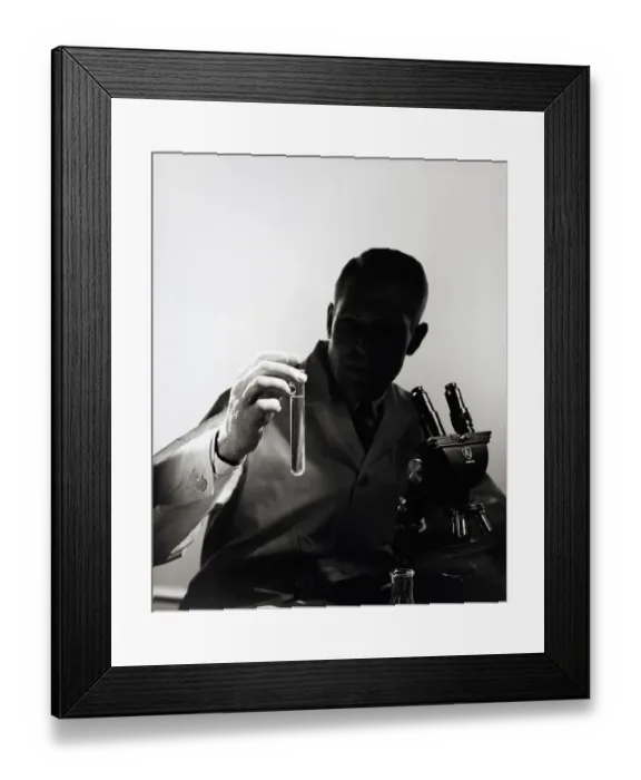 Framed Print : Male scientist wearing lab coat, sitting in darkness behind microscope Framed Print : Male scientist wearing lab coat, sitting in darkness behind microscope