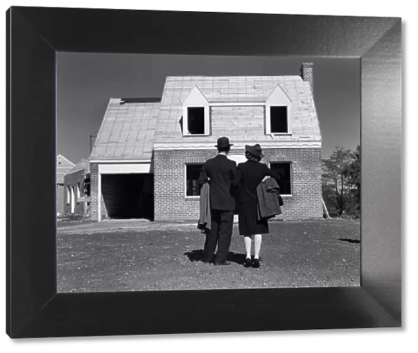 Couple looking at brick house under construction, rear view