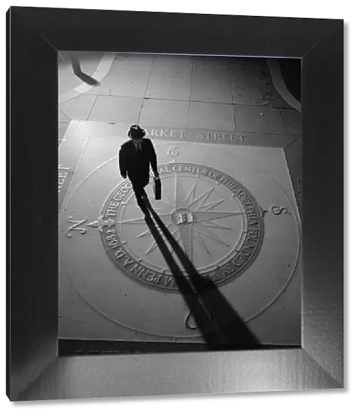 Silhouetted businessman with briefcase walking across compass in the sidewalk