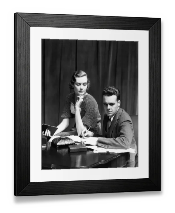 Framed Print : Couple Working On Budget At Desk Woman Sitting On Arm Of Chair Man With Pencil Writing On Framed Print : Couple Working On Budget At Desk Woman Sitting On Arm Of Chair Man With Pencil Writing On