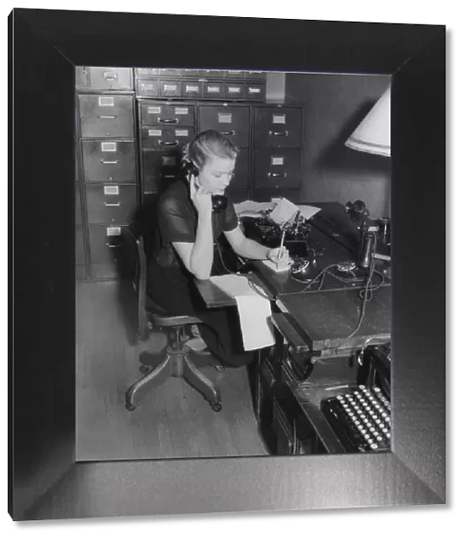 Secretary sitting at desk behind typewriter, on phone taking message