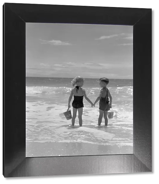 Boy and girl standing on beach, holding hands, rear view