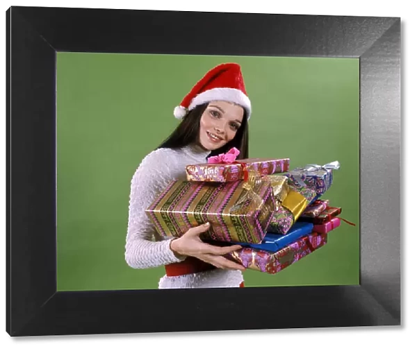 Young woman wearing santa hat, holding armful wrapped presents