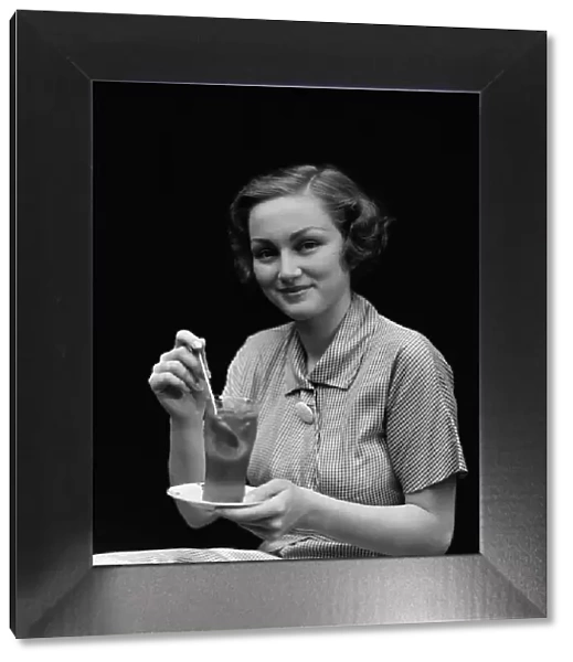 Woman in checked dress, stirring a glass of iced tea, portrait