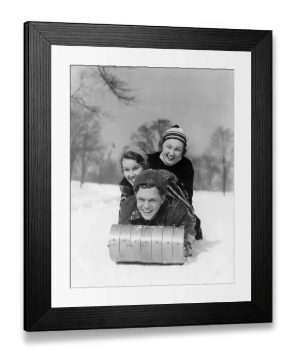 Framed Print : Man And Two Women Wearing Wool Hats And Winter Clothing Tobogganing In Snow With Tree
