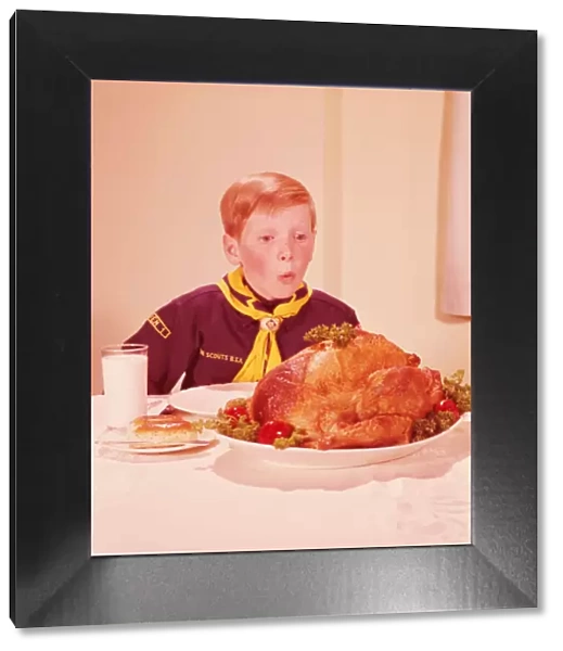 Boy in cub scout uniform looking hungrily at turkey on table. (Photo by H