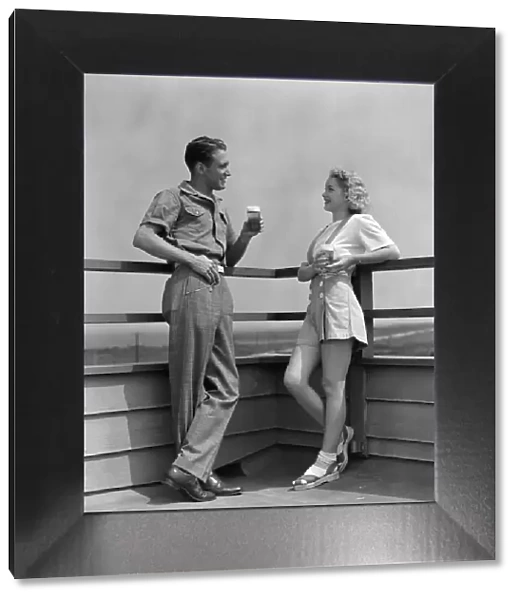 Man and woman smiling at each other, standing outside leaning against railing