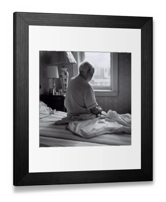 Framed Print : Senior man sitting on bed facing window Framed Print : Senior man sitting on bed facing window