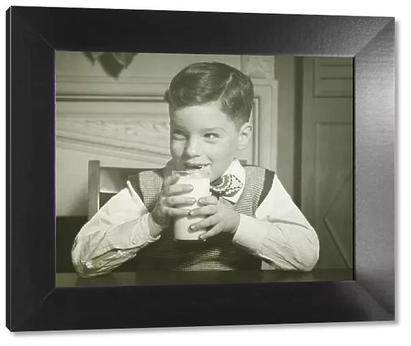 Boy (8-9) holding glass of milk, sitting at table, smiling, (B&W), close-up