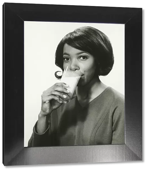 Young woman drinking milk in studio, smiling, (B&W), portrait
