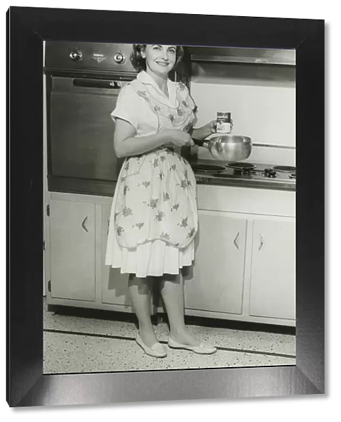 Young woman holding can of soup and pot in kitchen, (B&W)