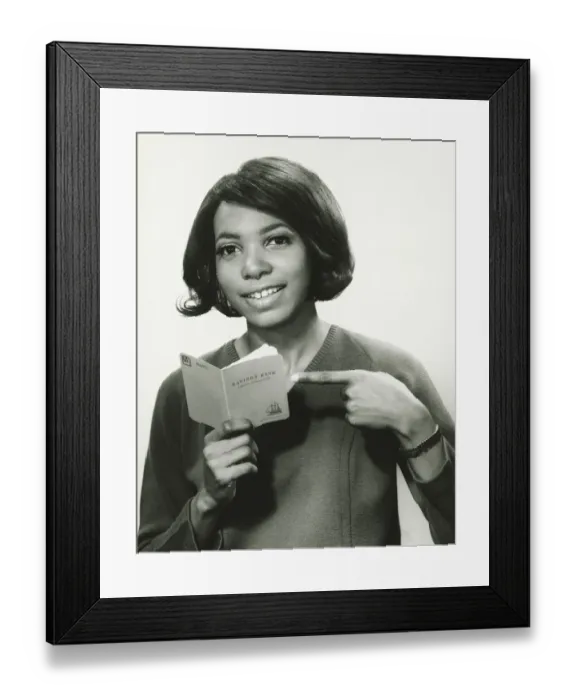 Framed Print : Young woman pointing at bank book, smiling, (B&W), portrait Framed Print : Young woman pointing at bank book, smiling, (B&W), portrait