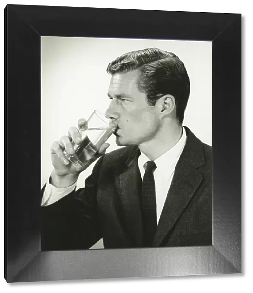 Young businessman drinking water, in studio, (B&W), portrait