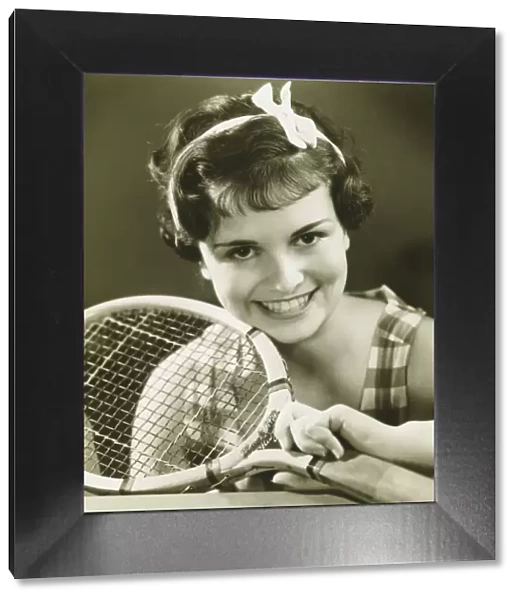 Young woman holding tennis racket, smiling, (B&W), portrait