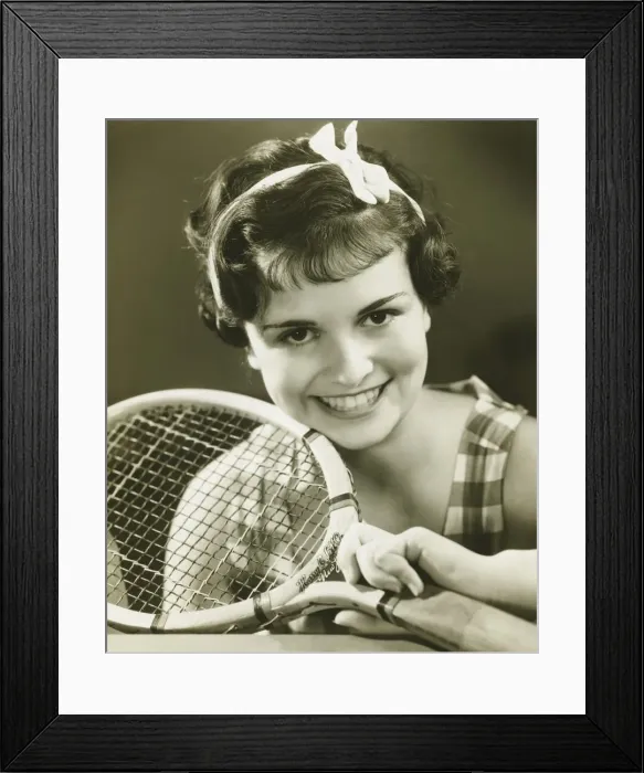 Framed Print : Young woman holding tennis racket, smiling, (B&W), portrait Framed Print : Young woman holding tennis racket, smiling, (B&W), portrait