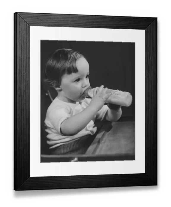 Framed Print : Baby girl (9-12 months) sitting in highchair, drinking milk from bottle (B&W) Framed Print : Baby girl (9-12 months) sitting in highchair, drinking milk from bottle (B&W)
