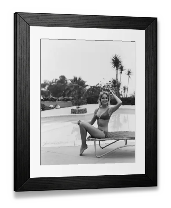 Framed Print : Young woman sitting on sun lounger by swimming pool, smiling, portrait Framed Print : Young woman sitting on sun lounger by swimming pool, smiling, portrait