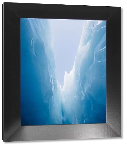 Looking up at the blue sky from deep with in a glaciers jagged crevasse