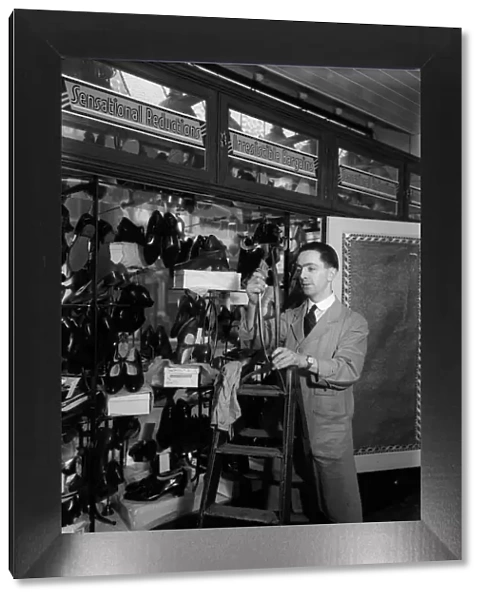 Shoe Sale. circa 1930: An assistant dressing a window for a shoe sale