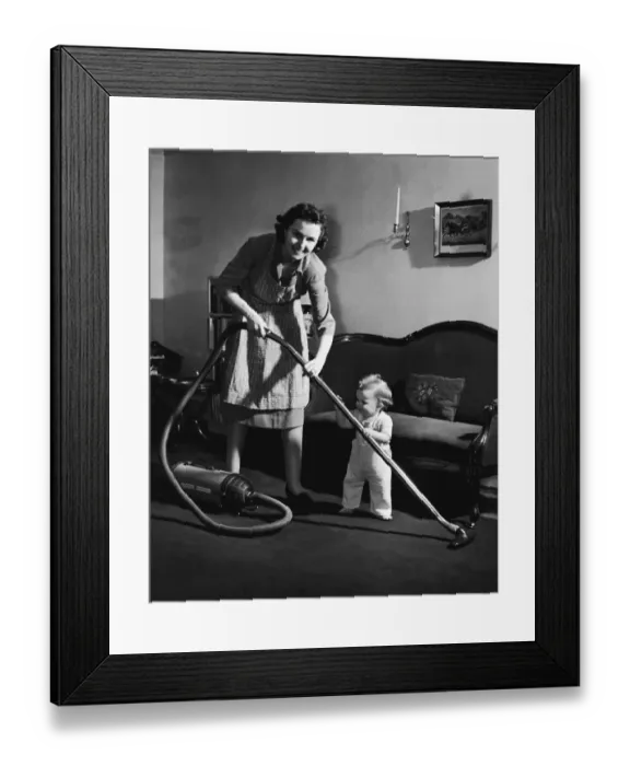 Framed Print : Mother and baby boy (12-15 months) holding vacuum cleaner (B&W) Framed Print : Mother and baby boy (12-15 months) holding vacuum cleaner (B&W)