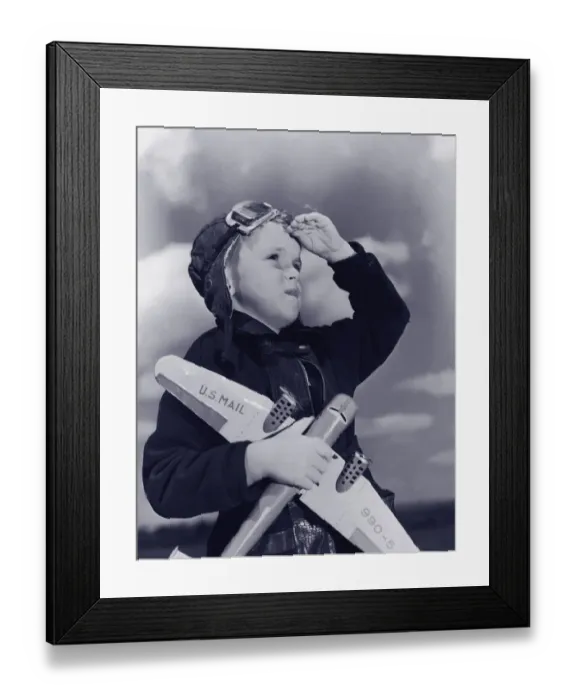 Framed Print : Boy (8-10) wearing flying cap and goggles holding toy plane (B&W)
