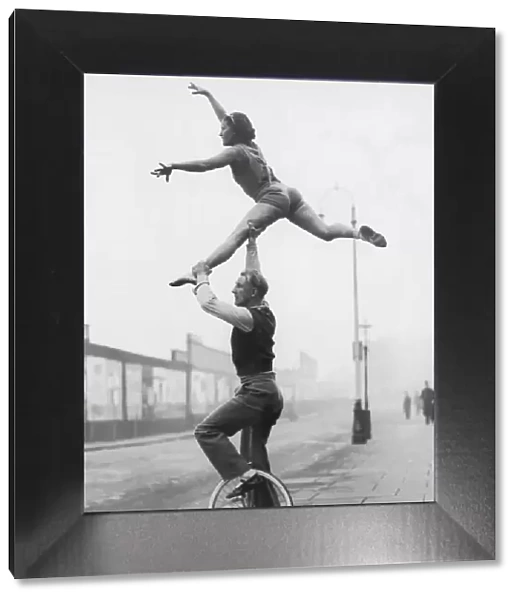 Male acrobat on unicycle supporting woman in air (B&W)