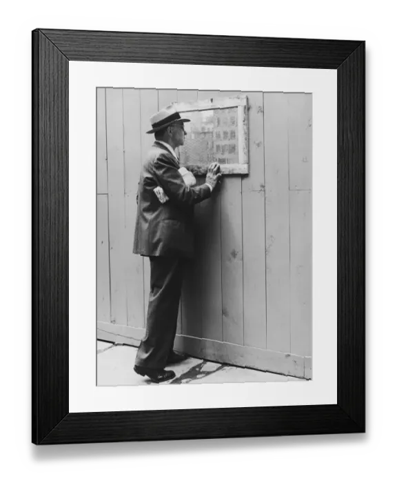 Framed Print : Mature man looking through window in fence at construction site (B&W) Framed Print : Mature man looking through window in fence at construction site (B&W)