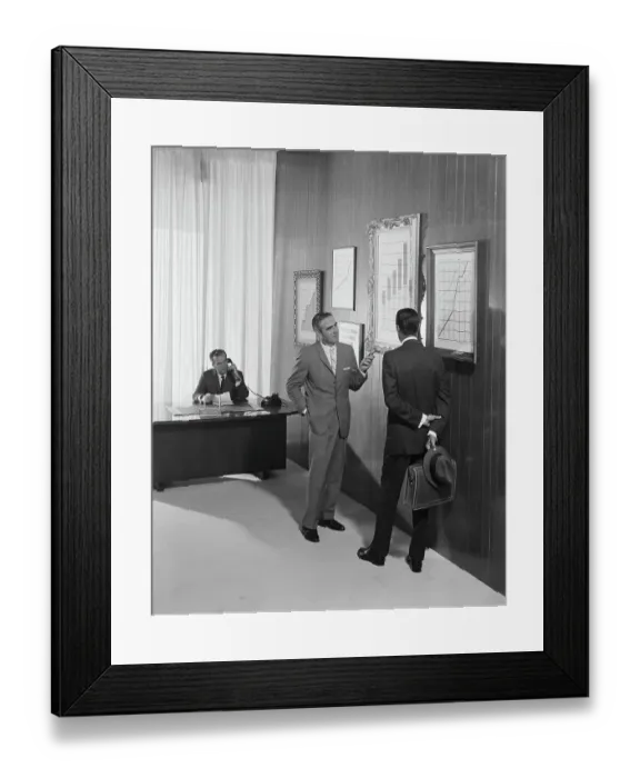Framed Print : Two businessman discussing at bar chart while another man using telephone in background Framed Print : Two businessman discussing at bar chart while another man using telephone in background