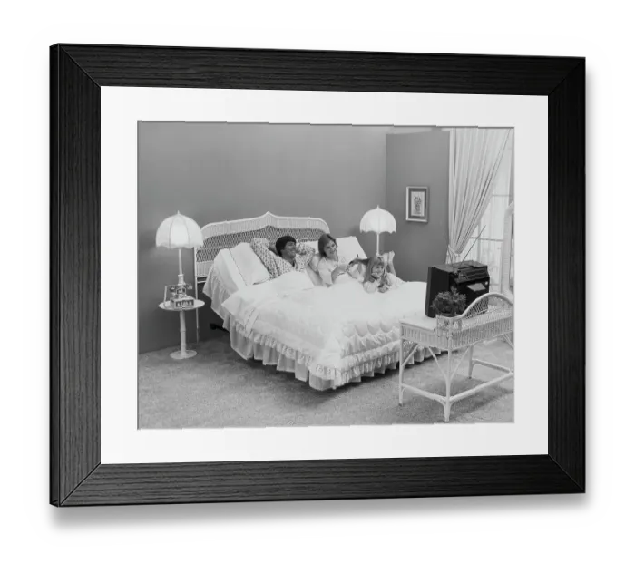 Framed Print : Father and mother with daughter lying on bed watching tv, smiling