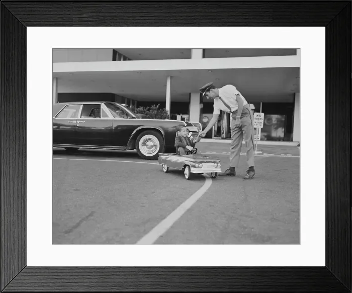 Framed Print : Boy sitting in toy car giving paper to traffic police officer Framed Print : Boy sitting in toy car giving paper to traffic police officer