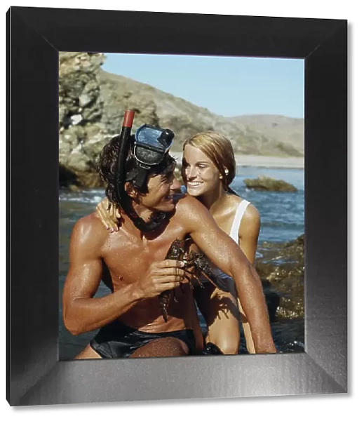 Man wearing snorkel, holding lobster beside woman, smiling