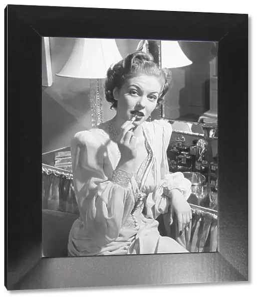 Woman sitting at vanity table, putting on lipstick, (B&W), portrait