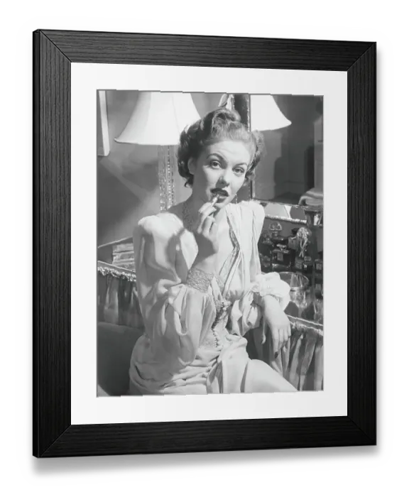 Framed Print : Woman sitting at vanity table, putting on lipstick, (B&W), portrait Framed Print : Woman sitting at vanity table, putting on lipstick, (B&W), portrait
