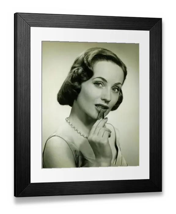 Framed Print : Woman applying lipstick in studio, (B&W), portrait