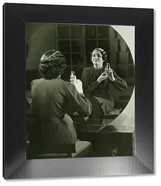 Young woman applying perfume in front of mirror, (B&W)