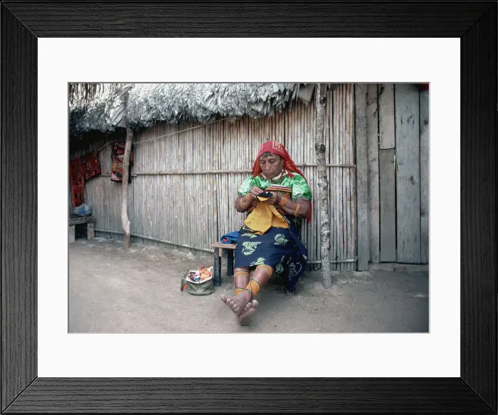 Framed Print : Woman Sits in Front of Hut Sewing Framed Print : Woman Sits in Front of Hut Sewing