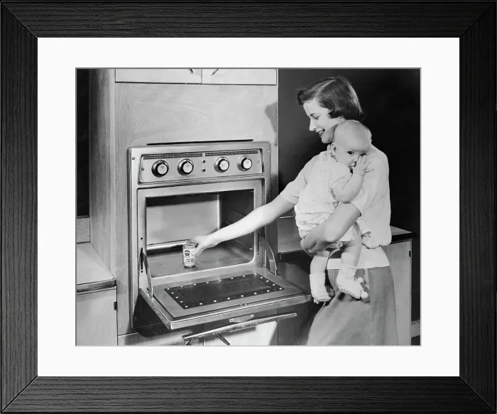 Framed Print : Woman with Baby Heating Up Food in New Oven Framed Print : Woman with Baby Heating Up Food in New Oven