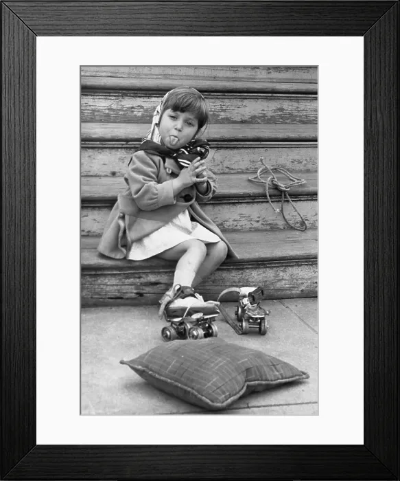 Framed Print : Girl (4-5) in roller skates sitting on stairs and sticking out tongue