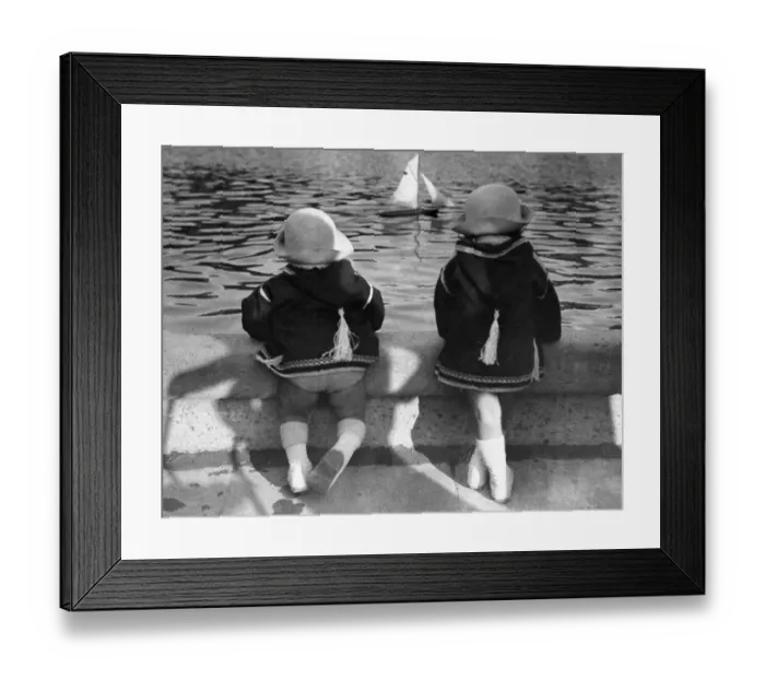 Framed Print : Twin girls (6-7) looking at model sailboat in pond Framed Print : Twin girls (6-7) looking at model sailboat in pond