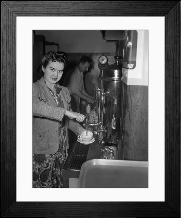Framed Print : Portrait of young woman using coffee machine, man in background