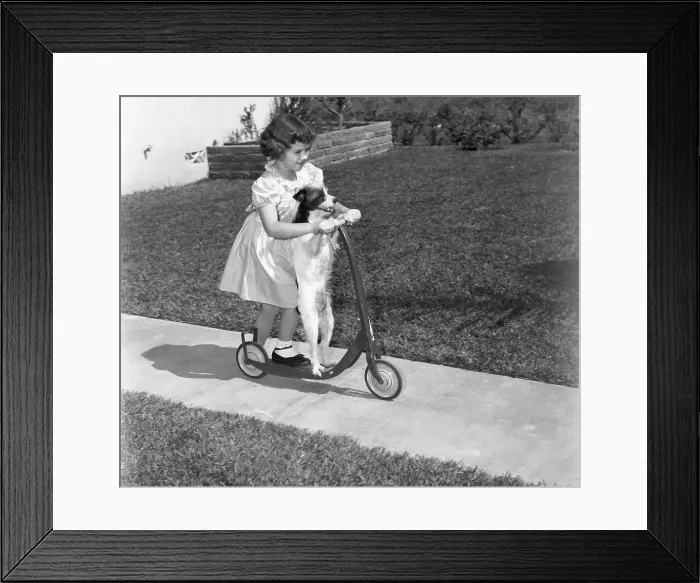 Framed Print : Girl (6-7) on scooter with dog