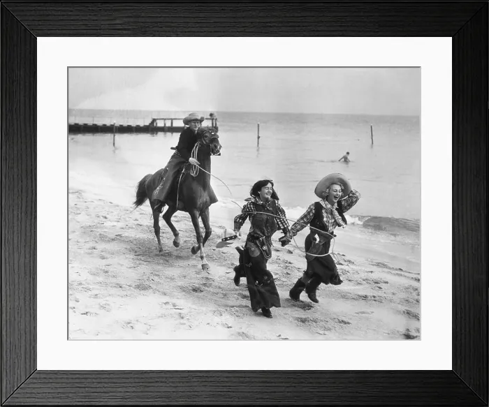 Framed Print : Cowboy on horse catching laughing women on beach