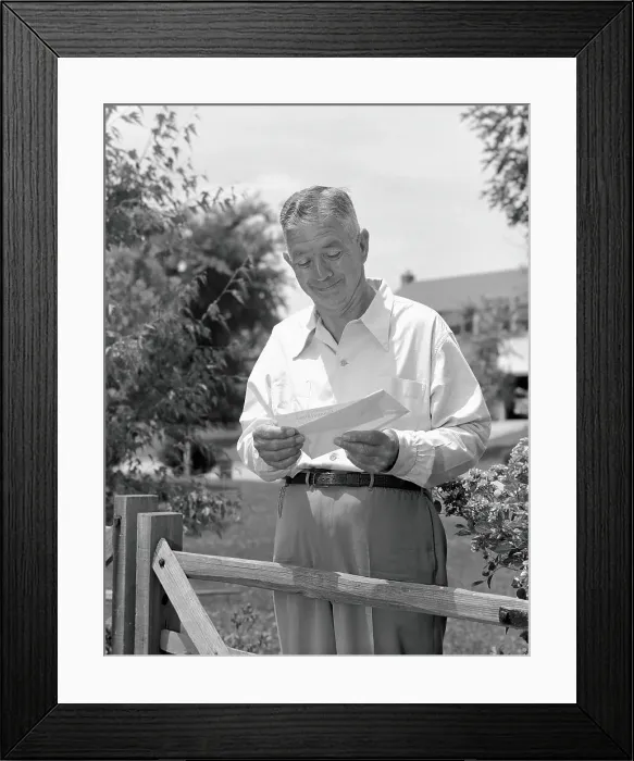 Framed Print : Elderly man standing by fence in yard, opening envelope and taking out cheque Framed Print : Elderly man standing by fence in yard, opening envelope and taking out cheque
