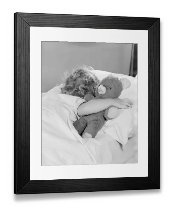 Framed Print : Little girl asleep in bed, with arm around teddy bear